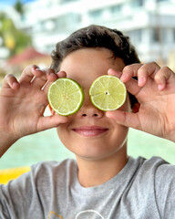 Young boy covering his eyes with lemons. Emotional kid boy. Cute boy at the summer time