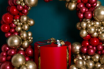 Arch of red and gold balloons on a green background. In the middle of the arch is a gift - a huge red box with a golden bow.