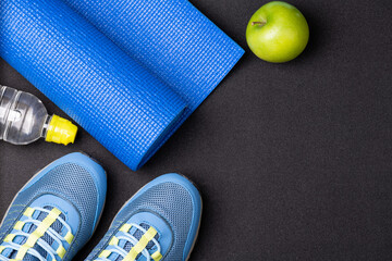 Sport shoes and equipment for fitness - healthy lifestyle, exercise, healthy food concept. Motivation sport card with sport equipment shoes, yoga mat, dumbbells, fruit and water on black background