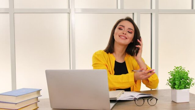 Smiling young business woman professional talking on phone using laptop sit at home office desk, happy female customer make mobile call confirming online website shopping order delivery concept
