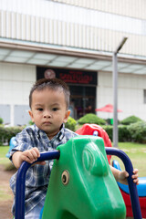 Asian toddler ride on pony toy in the park, looking into the camera 