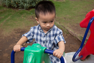 Asian toddler ride on pony toy in the park, looking into the camera 