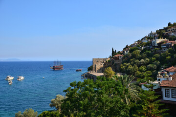 water edge with green trees, palms and houses and ancient ship on horizon on the sea