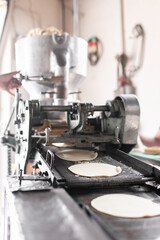 The conveyor belt of the nixtamall mill is producing corn tortillas