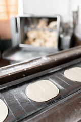 A gas stove conveyor belt is carrying some corn tortillas with the dough kneading machine in the...