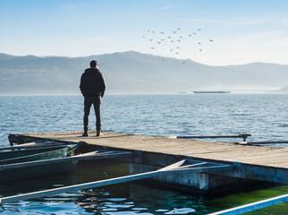 A man sits alone on a floating pontoon and contemplates the landscape. Meditation, dreaming,...