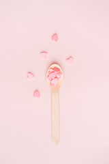 Wooden spoon with pink hearts on a pink background.