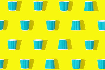 Creative pattern made of blue paper cups of coffee or tea to go on bright yellow background. Eco friendly concept. Flat lay. Top view