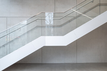 Side interior view of white staircase , glass and metal railing, and background of granite stone wall. 