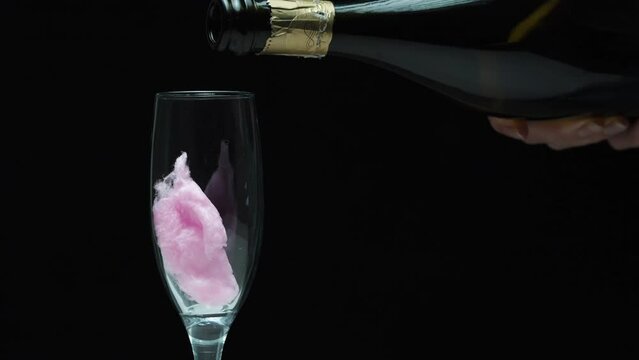A romantic drink, I put pink cotton candy in a glass and pour champagne. On a black background, close-up.