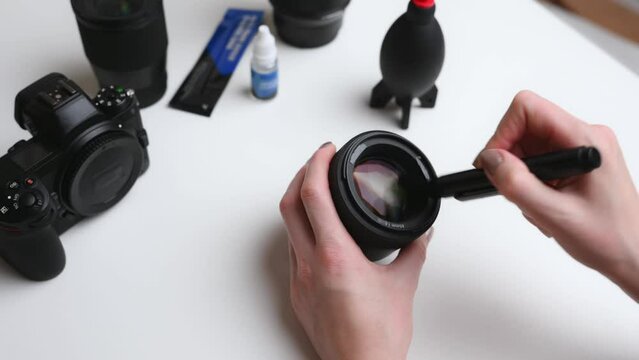 Cleaning the lens of a digital camera from dust with a special cleaning brush. The concept of caring for photographic equipment, cleaning the camera lens. The photographer cleans the lens.