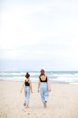 Fototapeta na wymiar Happy family on beach vacation. Back view of mother and little daughter are walking together and holding hands on beach. Mom and child girl kid enjoy and having fun at summer holidays
