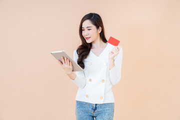 Portrait of a happy girl showing red credit card while holding mobile tablet isolated over orange background