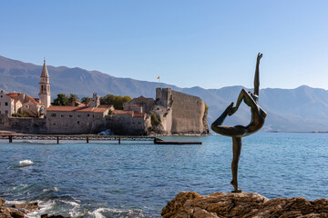 Ballerina statue (dancing girl) with panoramic view of the medieval old town of the coastal city of Budva, Montenegro, Adriatic Mediterranean Sea, Montenegro, Balkan, Europe. Dinaric Alps in the back - obrazy, fototapety, plakaty