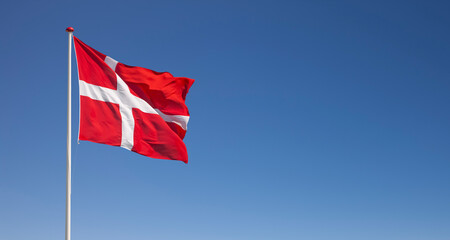 Dänische Nationalflagge im Wind wehend vor blauem Himmel