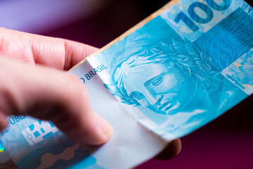 Um homem segurando notas do Real Brasileiro em sua mão. Economia brasileira, finanças e salário.