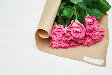 Delightful bouquet of purple roses with large buds and an amazingly aroma is packed in paper on light background. Bouquet of pink fresh cut roses wrapped in beautiful paper and tied with ribbon