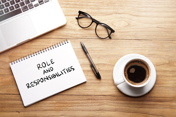 Role and Responsibilities, motivational words and sentences for work and life. Quote sentence in notebook with laptop, pen, coffee over wooden background.