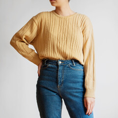 Woman wearing yellow sweater and blue mom jeans isolated on white background.