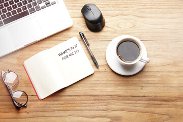 Whats In It For Me, motivational words and sentences for work and life. Quote sentence in notebook with laptop, pen, coffee over wooden background.