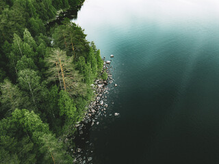 Aerial view of blue lake stone shore and and green woods with pine trees in Finland.