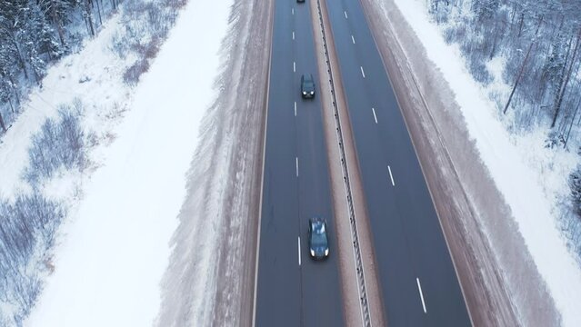 A white car is parked on a snowy roadside with emergency lights, high speed cars pass by on the road and do not stop in the middle of a forest covered with cold snow