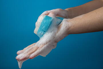 Women's hands in soapy foam on a blue background. Hand washing and hygiene concept.