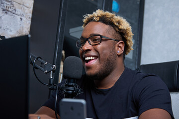 Fototapeta na wymiar A close up in the frame is the smile of a black guy in a black T shirt and glasses, sitting in front of a laptop screen. A handsome man sings a popular song into the microphone in his home studio