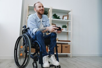 A man in a wheelchair gamer plays games with a joystick in his hands at home, copy space, with...