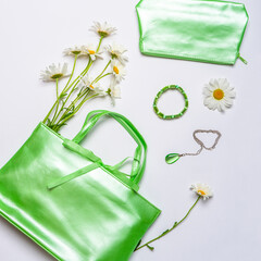 Stylish feminine handbag, cosmetic bag and jewellery with daisy flowers on white background. Female accessories in green pastel color. Spring or summer fashion concept. Flat lay, top view, copy space