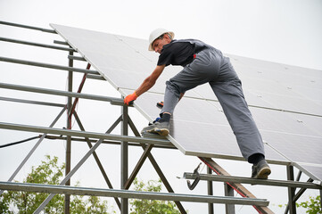 Man technician installing photovoltaic solar panels. Male worker in safety helmet placing solar...