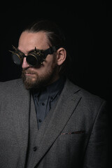 Obraz premium charismatic man in a classic suit and steampunk goggles on a black background stylish Portrait