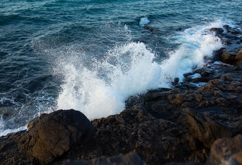 View of beautiful storm waves splashing into volcanic lava rocks at Costa Teguise coastline. Colorful seascape with spray of waves rolling into volcano stones. Lanzarote, Canary Islands, Spain.