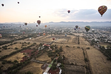 Landscape of sunrise with hot air balloons rising over fields and ancient teotihuacán ruins outside of Mexico City