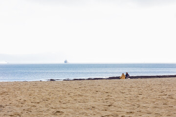 Fototapeta na wymiar Ocean coast couple sitting on the sand, cruise ship on the horizon