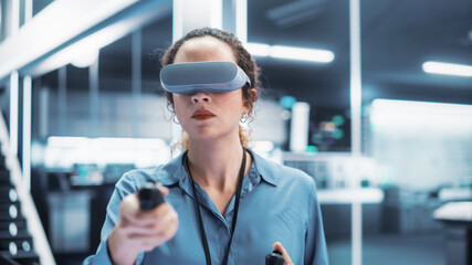 Portrait of a Female Engineer Using a Virtual Reality Headset with Controllers to Operatean Indsutrial Robot or Spend Time in Virtual Office Metaverse.