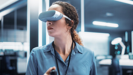 Portrait of a Female Engineer Using a Virtual Reality Headset with Controllers to Operatean Indsutrial Robot or Spend Time in Virtual Office Metaverse.