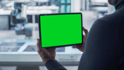 Robotics Engineer Using a Tablet Computer with Green Screen Mock Up Display Screen Running Augmented Reality. Robotic Arm Holding a Microchip. Automation Startup Research and Development Office.