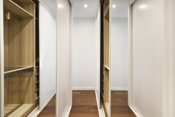 Dressing room of a bedroom with wardrobes with sliding doors with white wood and mirrors on both sides of the room