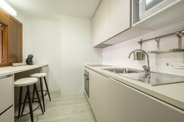Modern handleless kitchen with sink with stainless steel single-lever faucet and worktop with serving hatch with matching stools