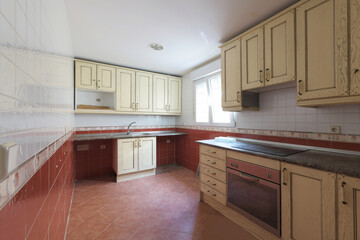 Kitchen with light wood cabinets with gray countertops and aluminum French windows, red and white tiles separated by a border and brown tile floors