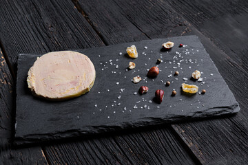 Traditional French foie gras on a slate with peppercorns, hazelnuts, salt and dried fruits