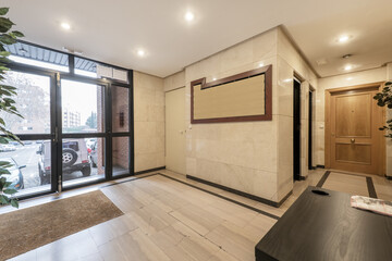 Lobby of a residential building with a table for the concierge, marble floors and walls, and oak doors