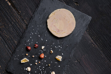 French foie gras on a slate served with nuts, pepper, salt, and dried fruits, top view - obrazy, fototapety, plakaty