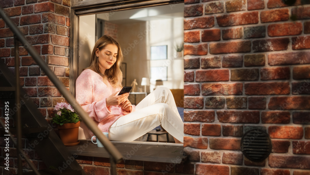 Aufkleber woman in pink comfy sweater using smartphone and drinking herbal tea while sitting on her windowsill