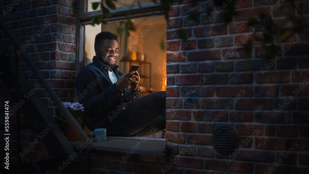 Poster black man using smartphone for online shopping while sitting on his windowsill at night. e-commerce 
