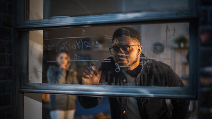 African American Young Man Using an Erasable Marker to Solve a Math Equation on Window Glass. Black...