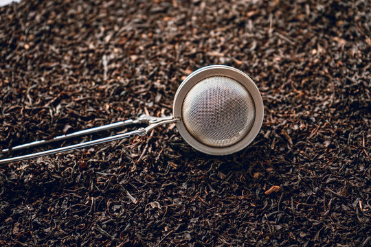 Metal tea strainer placed on dry leaves of tea