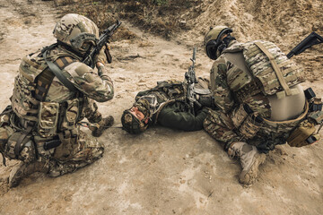 Fototapeta premium Wounded man lying on a ground, other soldiesr next to him
