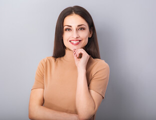 Beautiful young business toothy smiling woman in beige blouse thinking and looking happy on blue grey background with empty copy space. Portrait